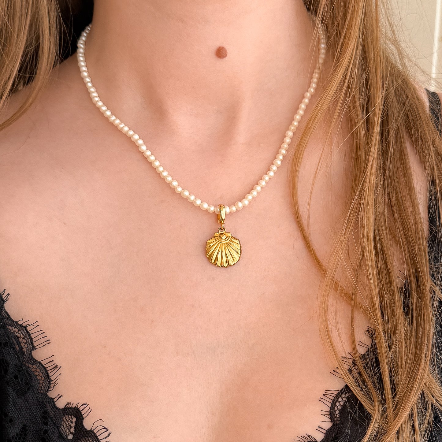 Pearl necklace with a gold shell pendant worn by a person in a black lace top.