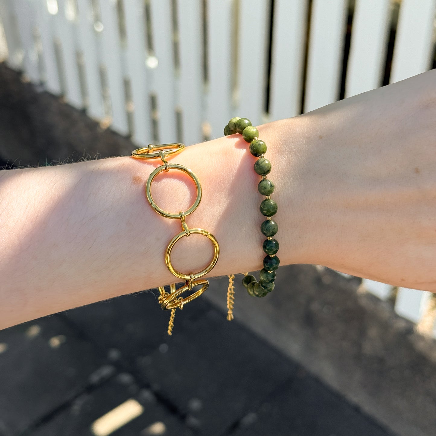 Gold and green bracelets on a wrist with a blurred background