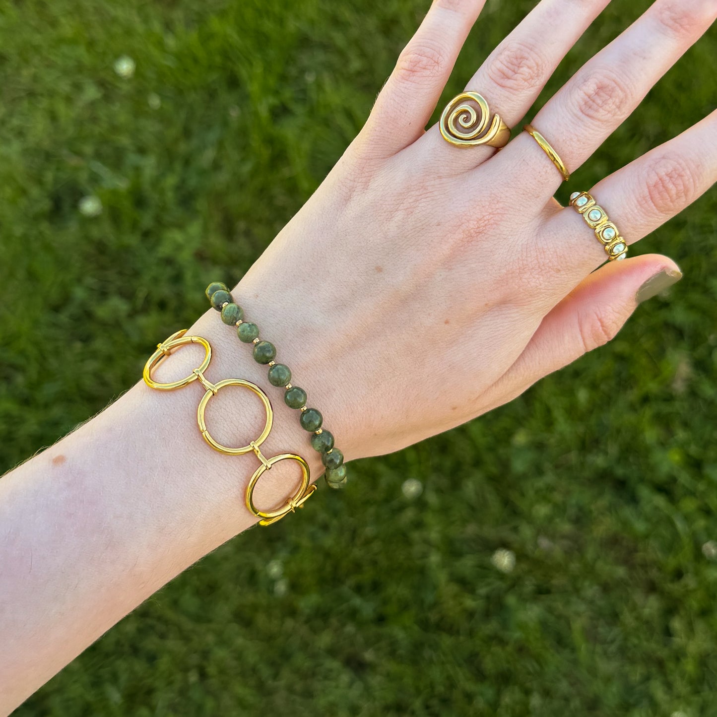 Hand wearing gold bracelet and rings against a grass background