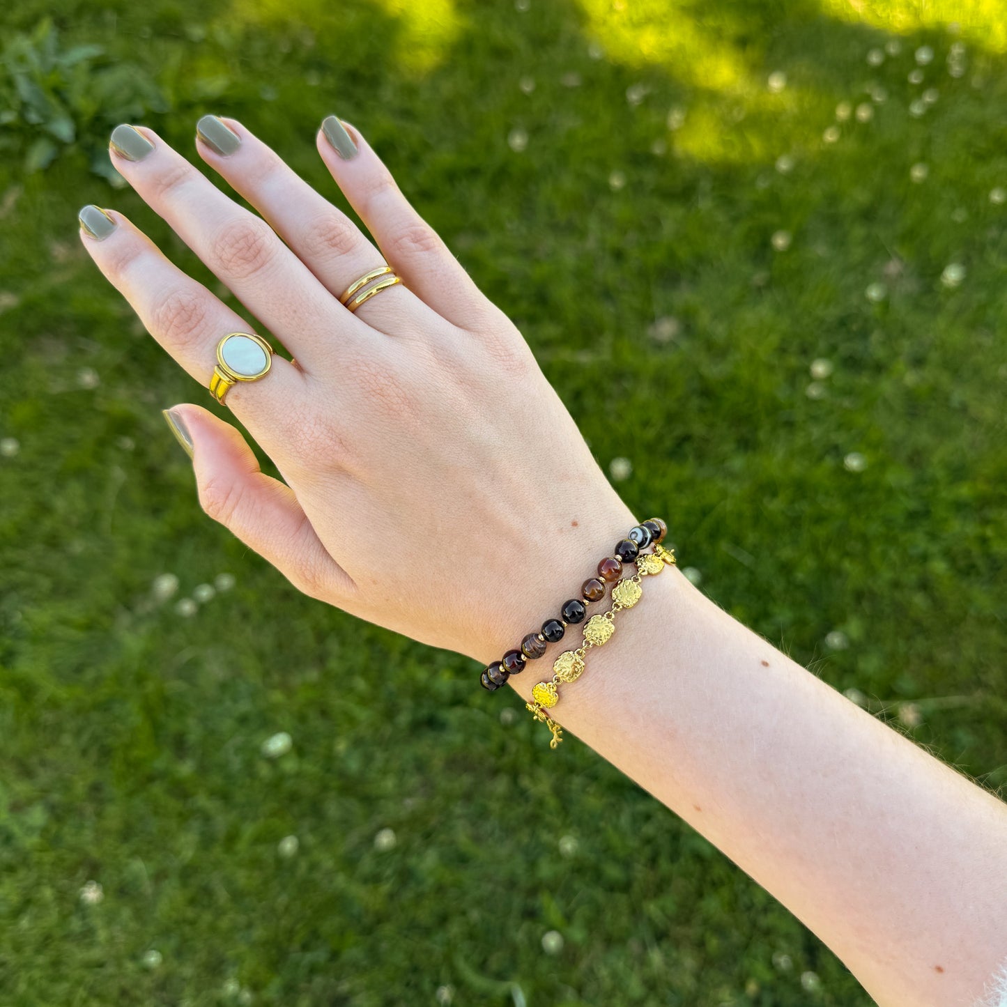 Hand wearing a ring and a brown beaded bracelet against a green grass background