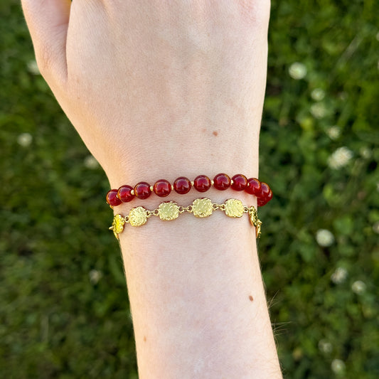 Bracelet with red beads and gold accents on a wrist against a grassy background