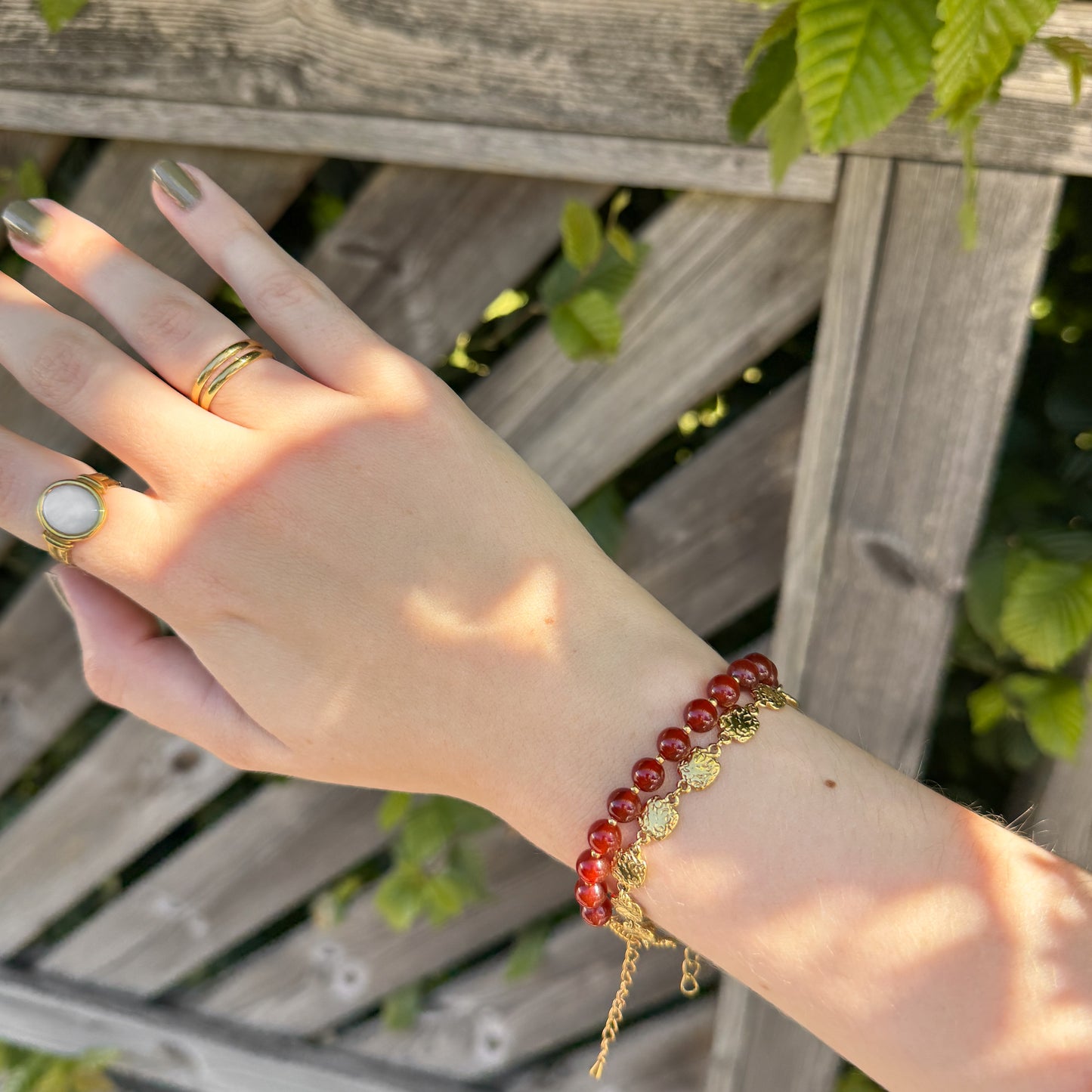 Hand wearing a red beaded bracelet with gold accents against a wooden background