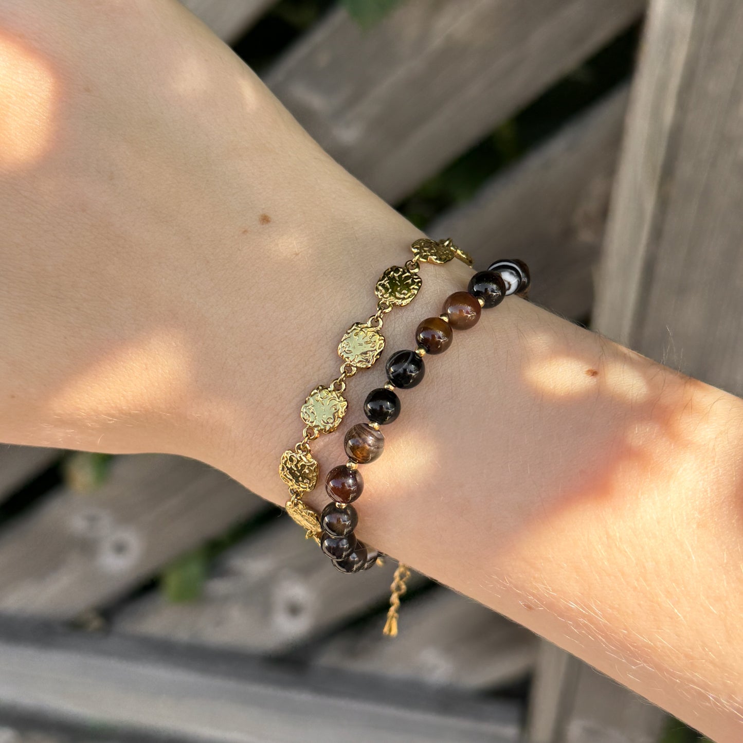 Close-up of a wrist wearing two bracelets with gold and beaded designs against a blurred background.
