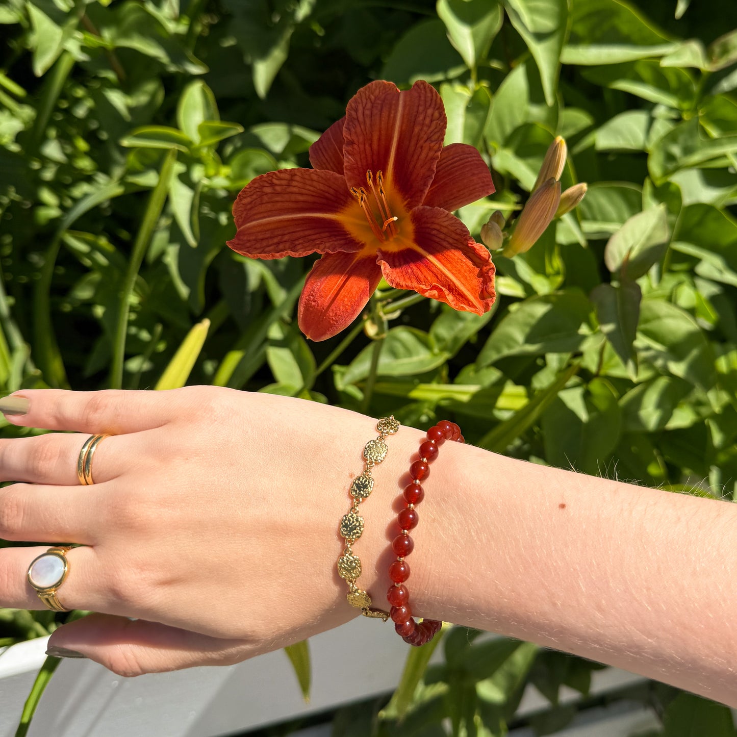 Hand wearing a red beaded bracelet with a red flower in the background.