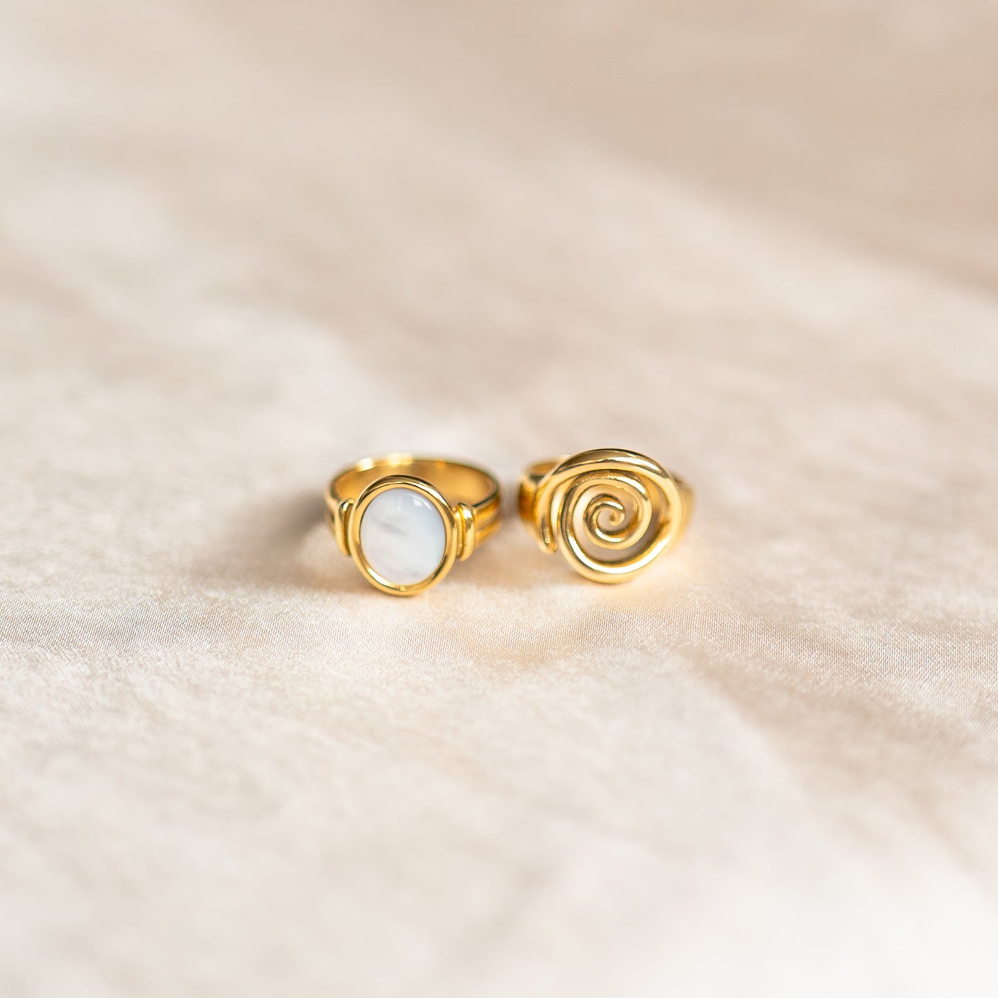 Two gold rings, one with spiral design on a beige fabric background