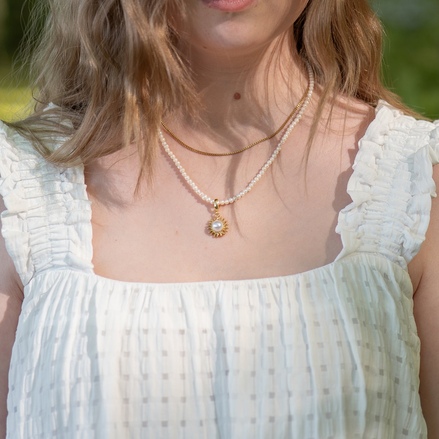 Woman wearing a white dress with a pearl necklace with the Solara Charm, outdoors