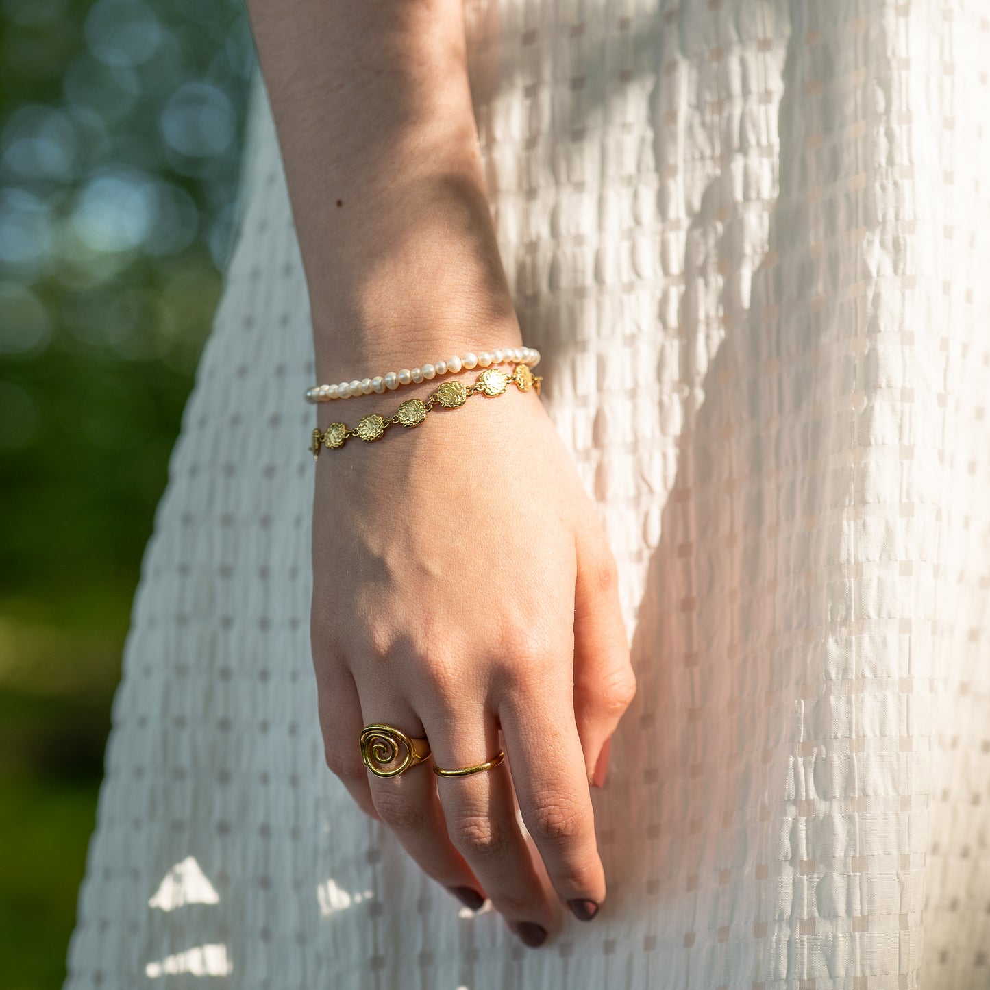Hand wearing gold rings and bracelets with a blurred natural background