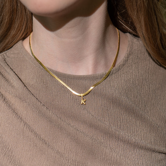 Gold "snake" necklace with a 'K' pendant worn by a person against a neutral background