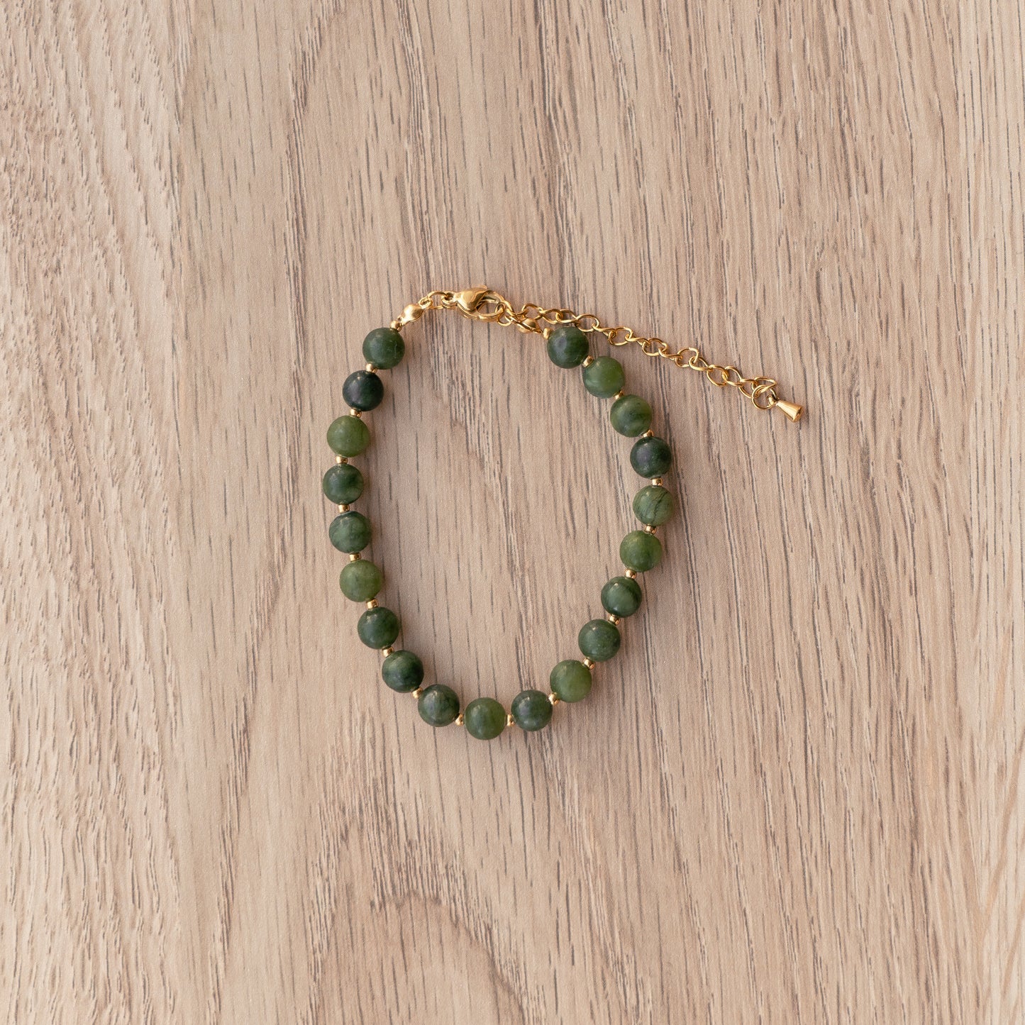 Green beaded bracelet with gold chain on a wooden surface