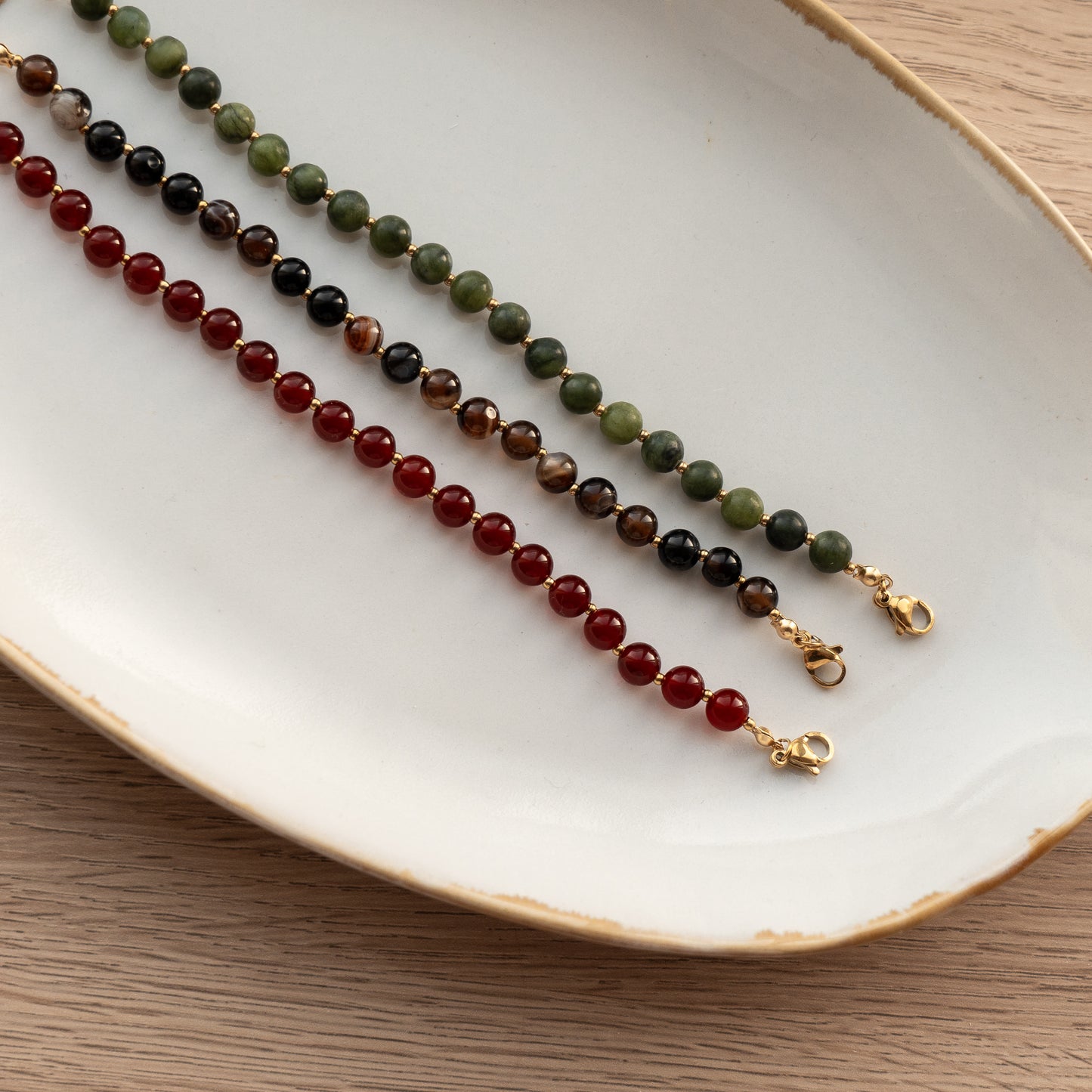 Three beaded necklaces on a white plate with a wooden surface underneath.