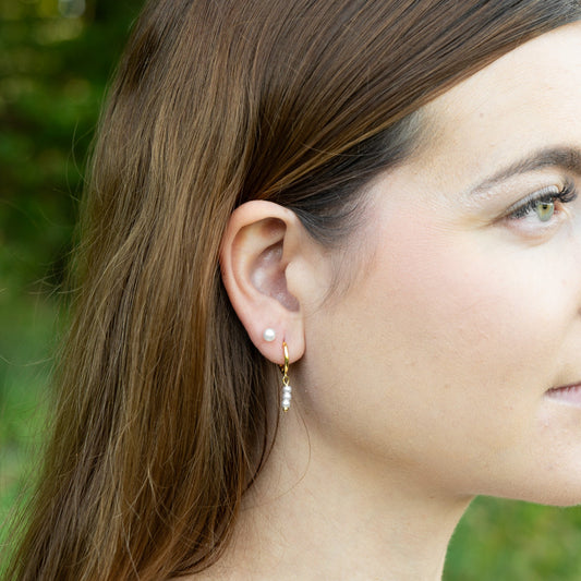 Close-up of a woman wearing pearl earrings with a blurred green background