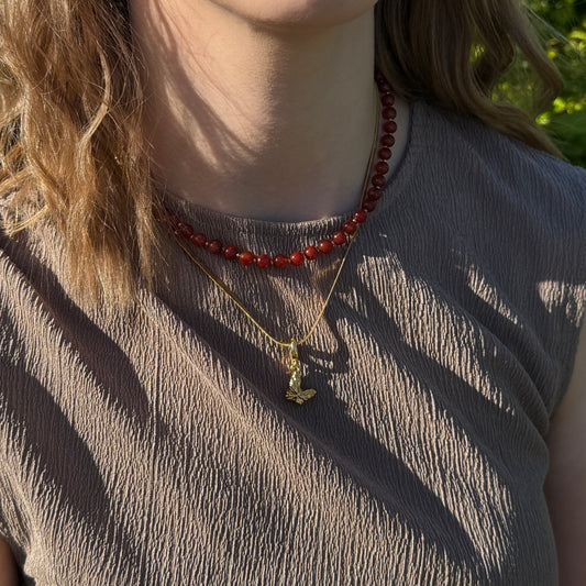 Person wearing a red beaded necklace and a gold pendant necklace.