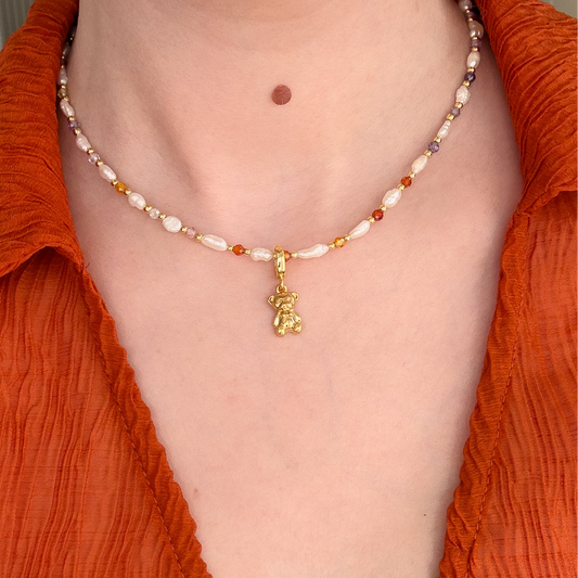 This image displays a charming necklace known as the "Teddy Charm". It features a delicate bead strand in shades of white freshwater pearls and gold pearls, interspersed with small, sparkling rhinestones.