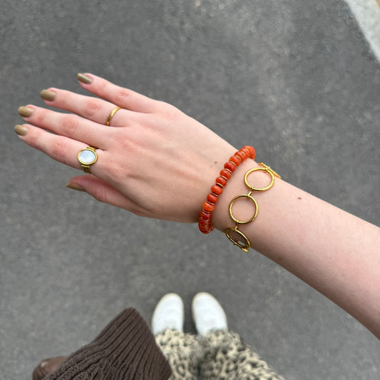 Hand wearing gold rings and bracelets on a gray pavement background