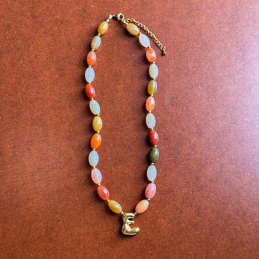 Beaded necklace with a letter 'E' charm on a brown background