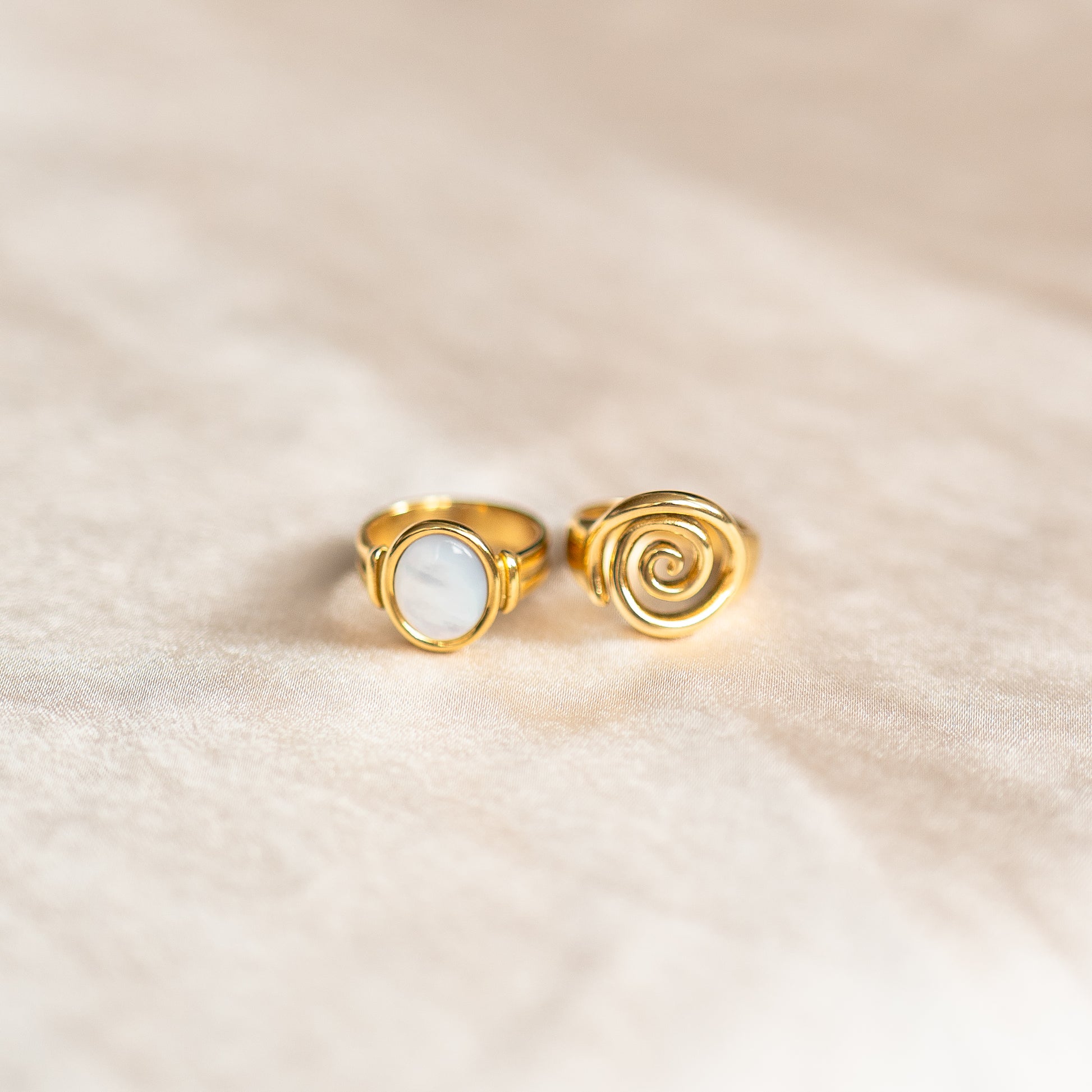 Two gold rings, one with spiral design on a beige fabric background