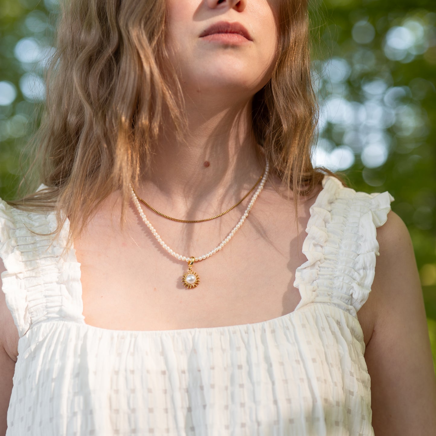 Woman wearing a freashwater pearl necklace with a pendant against a blurred green background 
