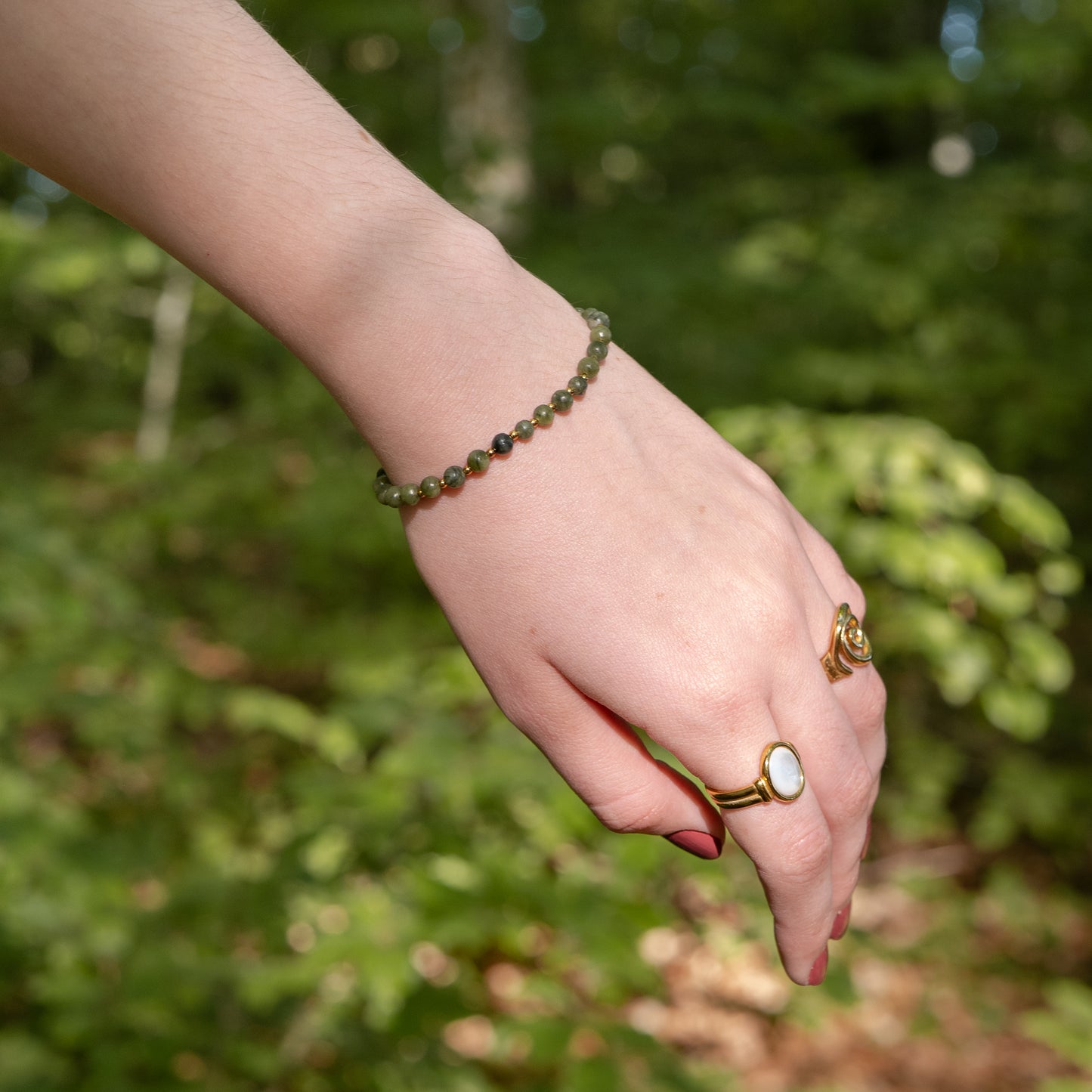 Hand wearing a green beaded bracelet and rings with a blurred green natural background