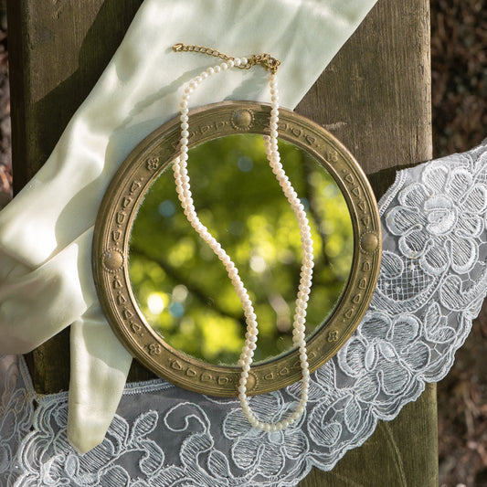 Freshwater pearl necklace draped over a round mirror on a lace tablecloth with a natural background