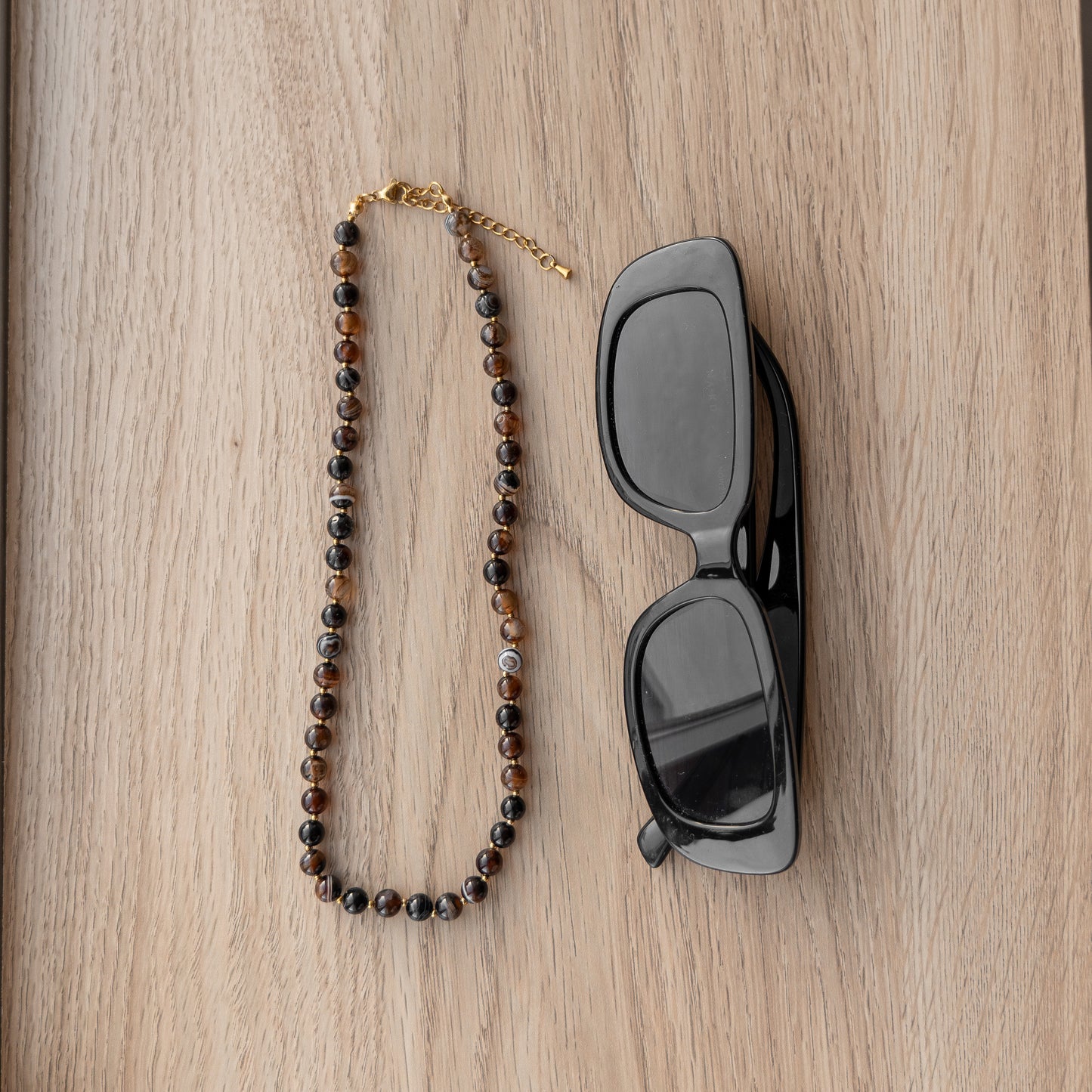 Brown beaded necklace and sunglasses on a wooden surface