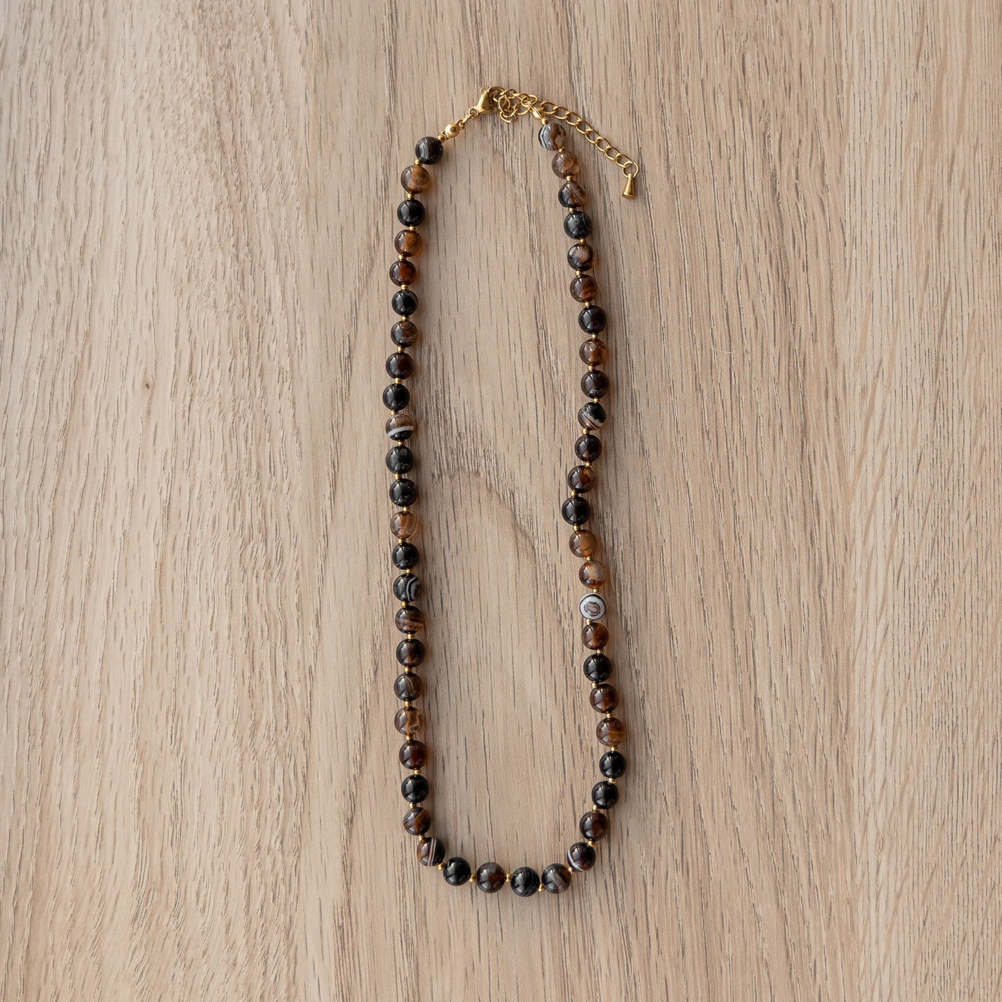 Brown beaded necklace with a gold chain on a wooden surface