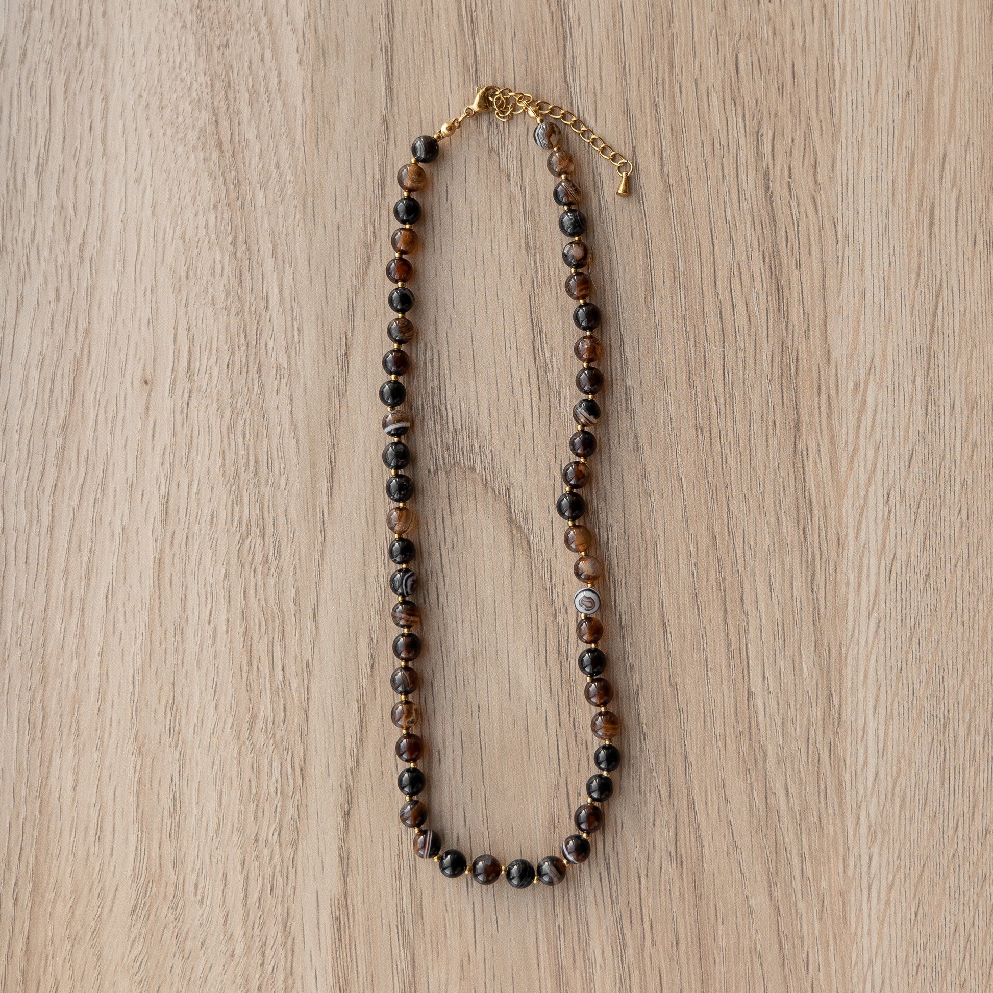 Brown beaded necklace with a gold chain on a wooden surface