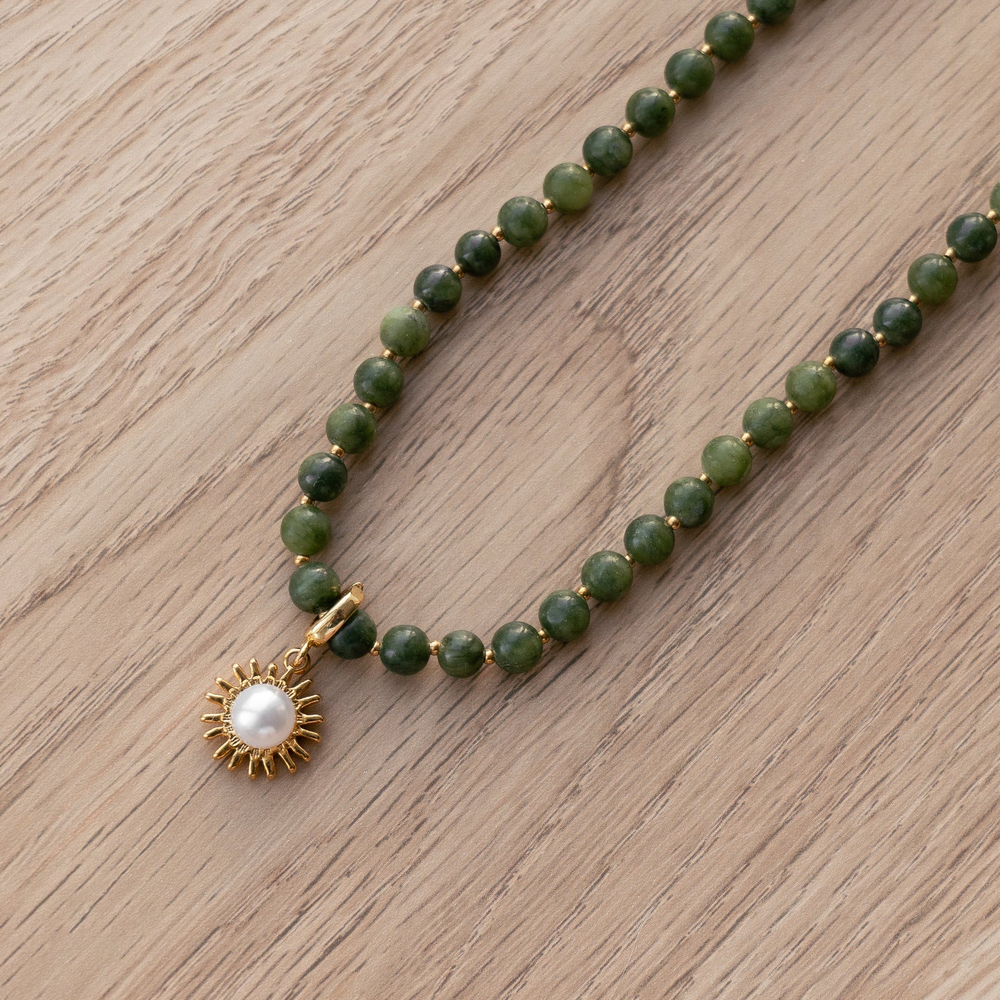Green beaded necklace with a gold sun pendant white pearl on a wooden surface