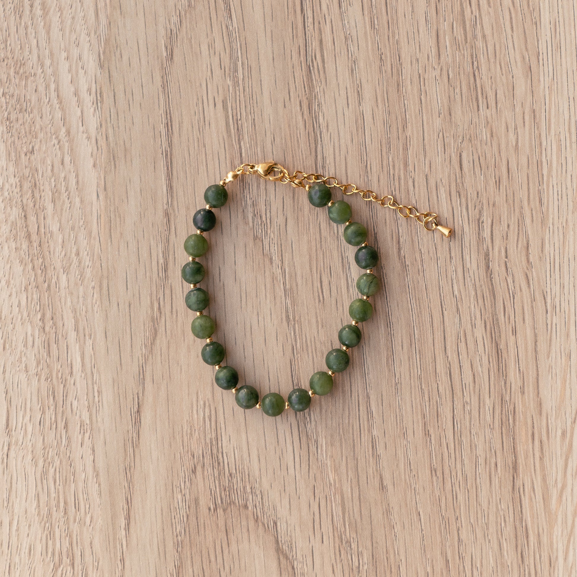 Green beaded bracelet with gold chain on a wooden surface