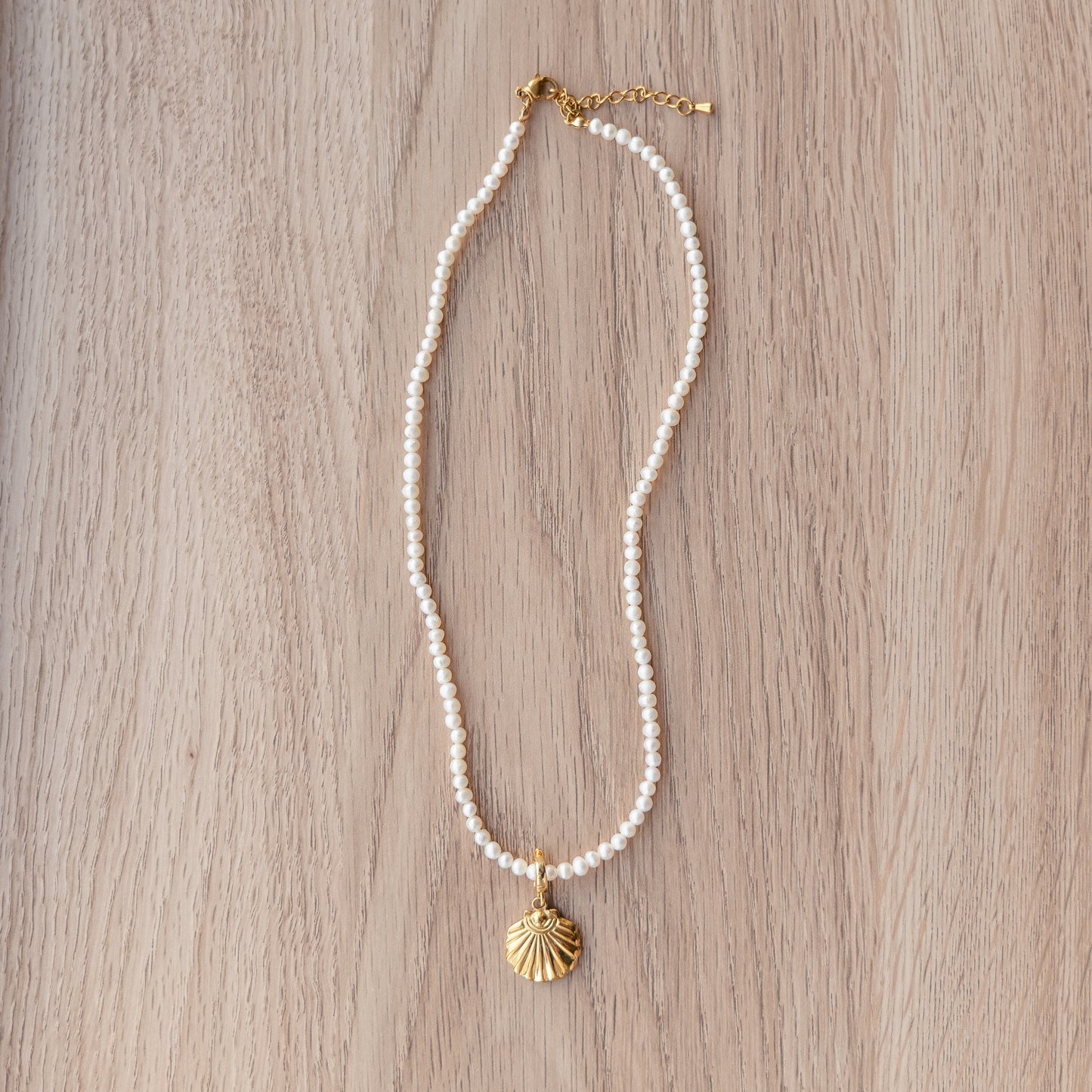 Pearl necklace with a gold shell pendant on a wooden surface.
