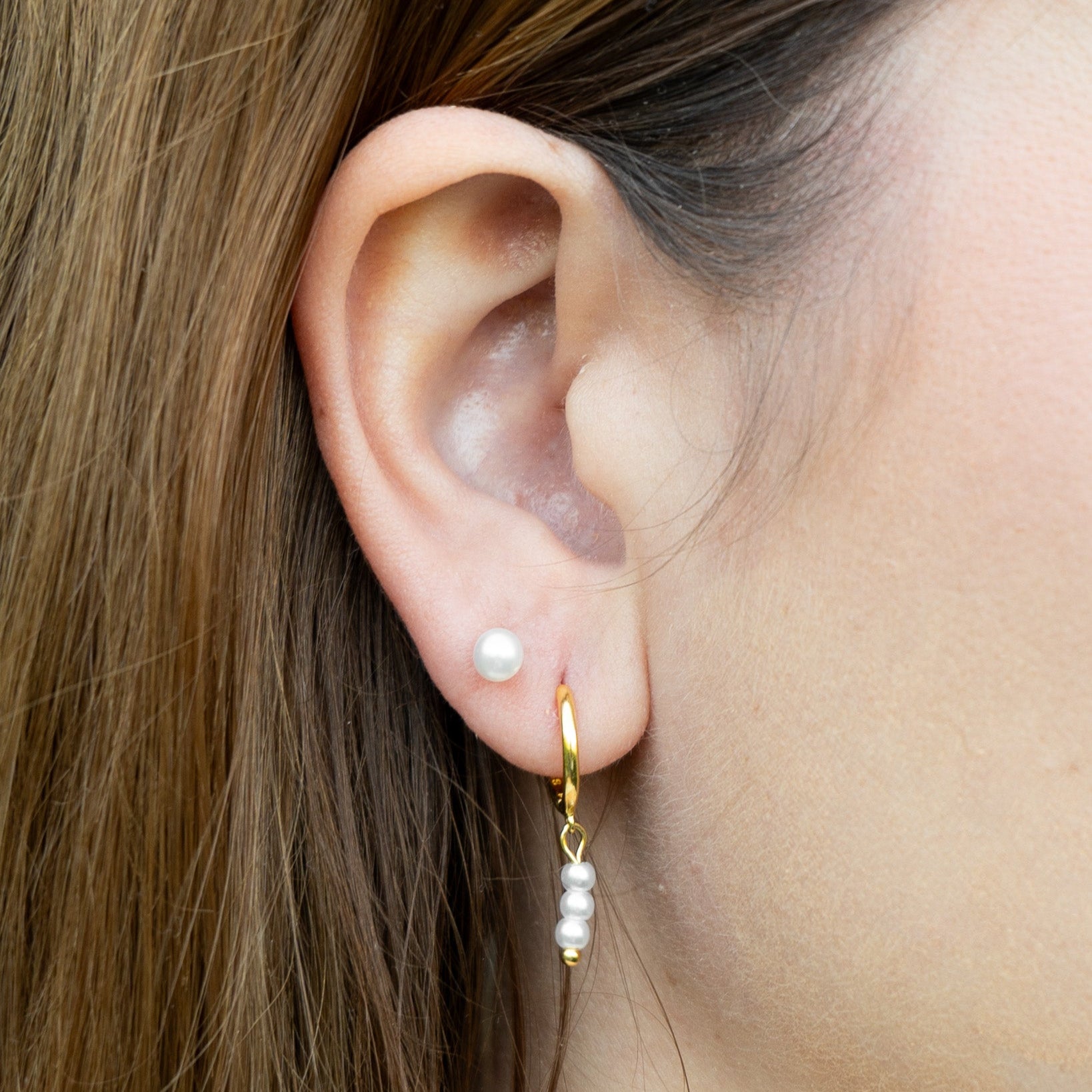 Close-up of an ear wearing a gold earring with pearls.