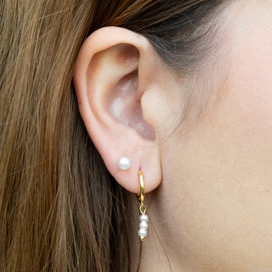 Close-up of an ear wearing a gold earring with pearls.