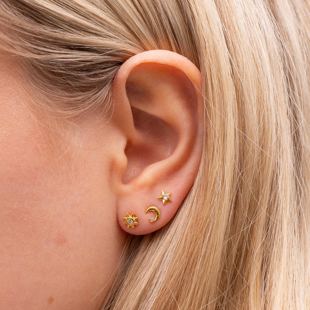 Close-up of an ear wearing gold earrings with a blurred background
